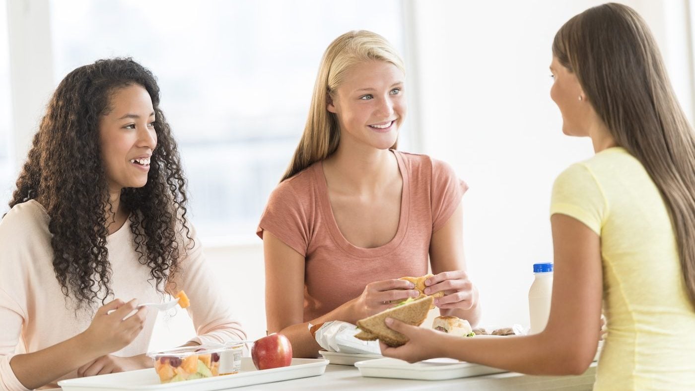 Three girls eating trays of food at cafeteria table