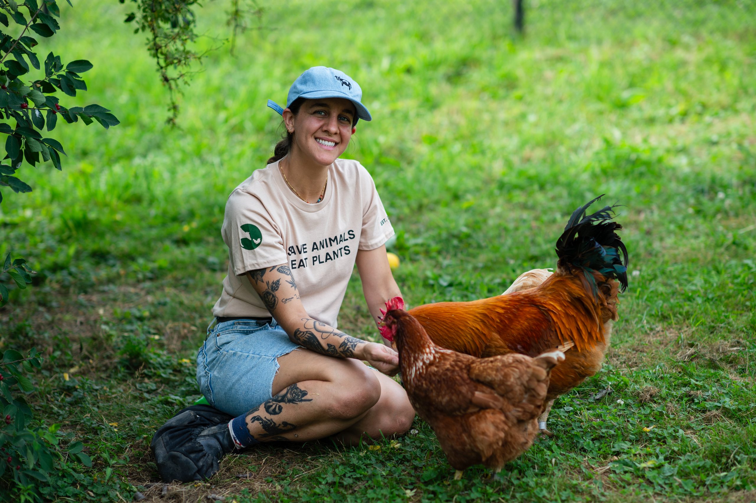 Two rescued chickens, and Farm Sanctuary staffmember Emily Grizzell wearing t-shirt that reads "Save animals, eat plants"