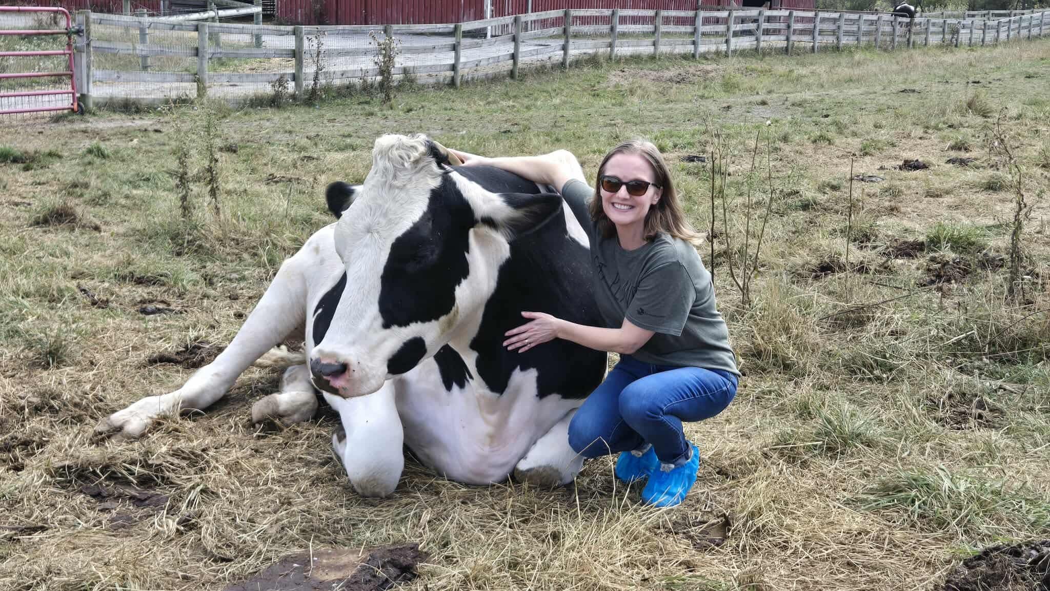 Farm Sanctuary Senior Manager, Education Program, Mercy Mize sits in pasture and hugs rescued cow