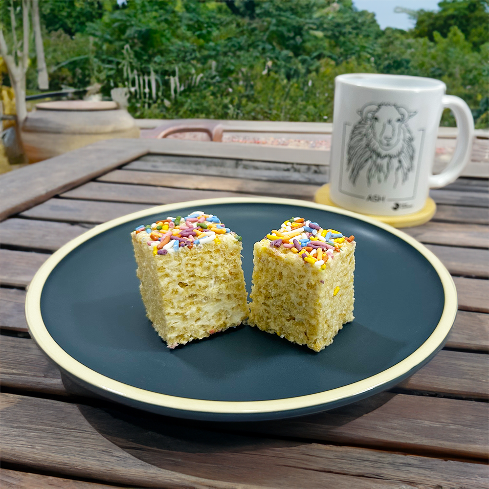 Two plated vegan rice krispie treats on table with sheep mug , in front of green garden