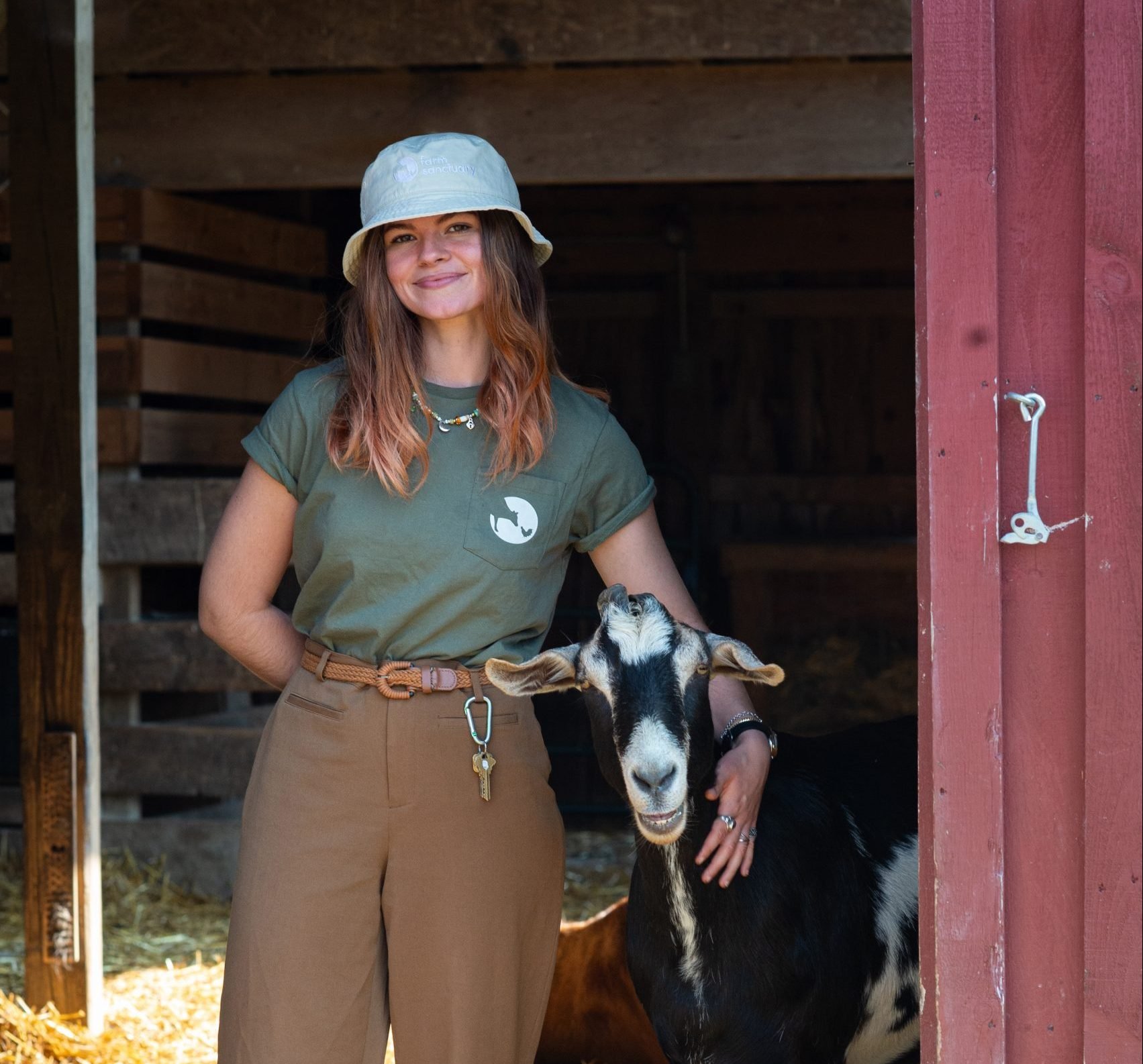 Farm Sanctuary staff Alice Scarpati wears green pocket logo tee and stands with rescued goat