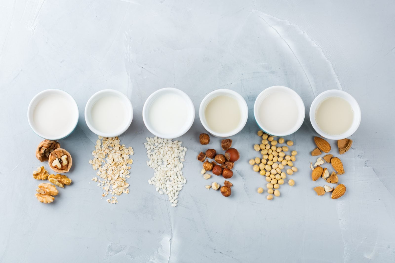 White cups of plant-based milk, each behind scattered nuts