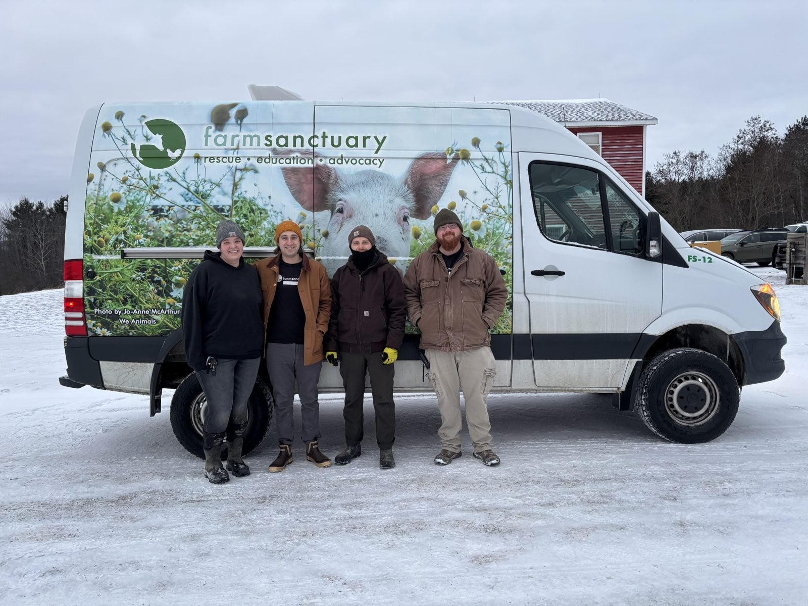Four staff members stand on ice in front of Farm Sanctuary van with a photo of a pig on it
