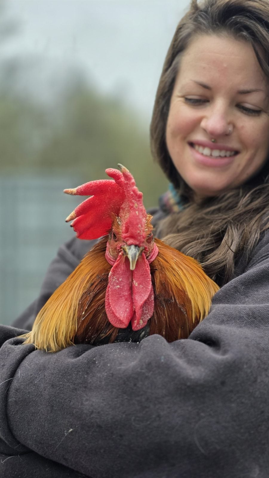 A smiling caregiver holds a rescued chicken in her arms
