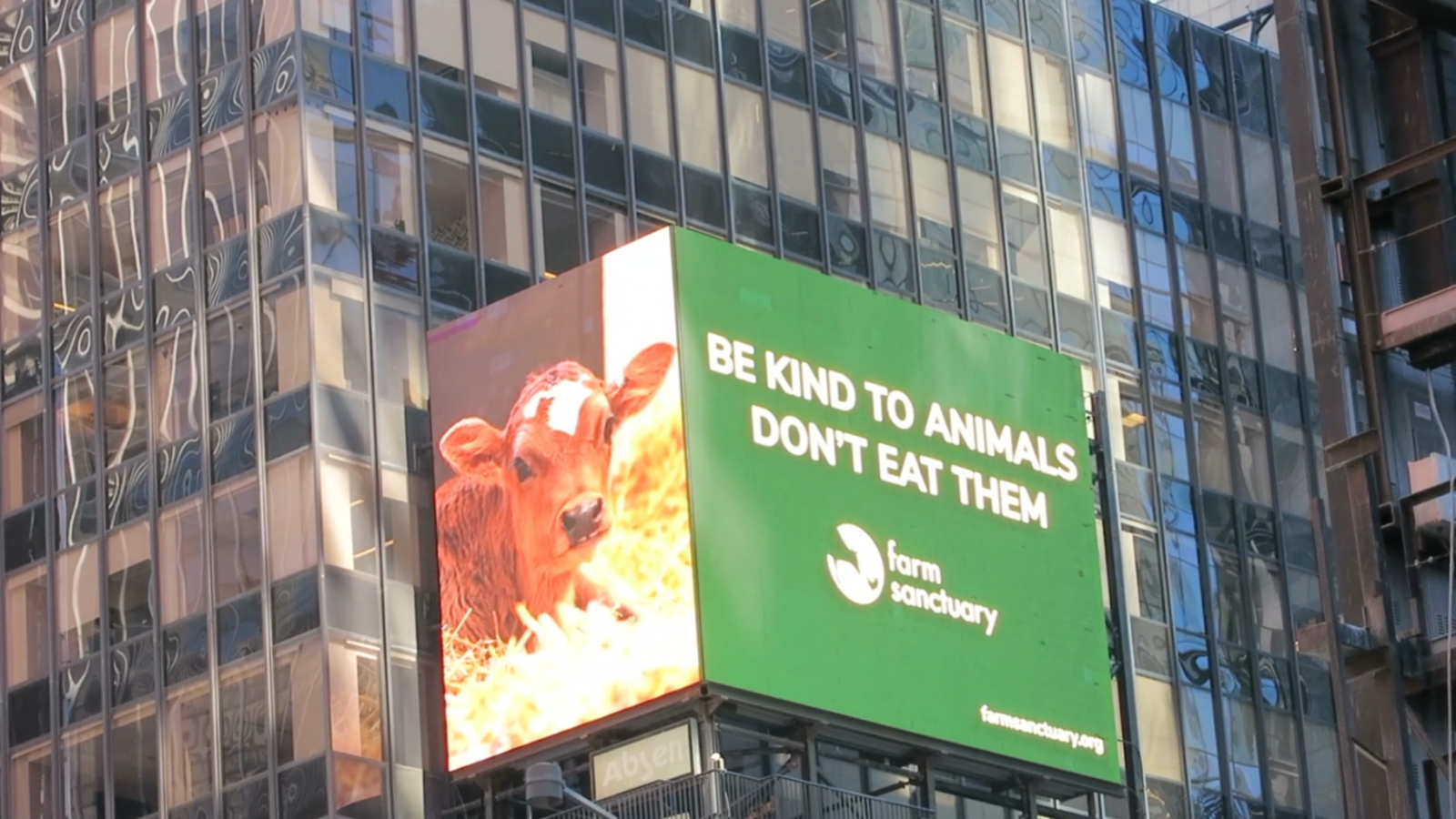 Billboard on tall building displays a rescued cow, and the words "Be kind to animals, don't eat them," and a Farm Sanctuary logo on green background