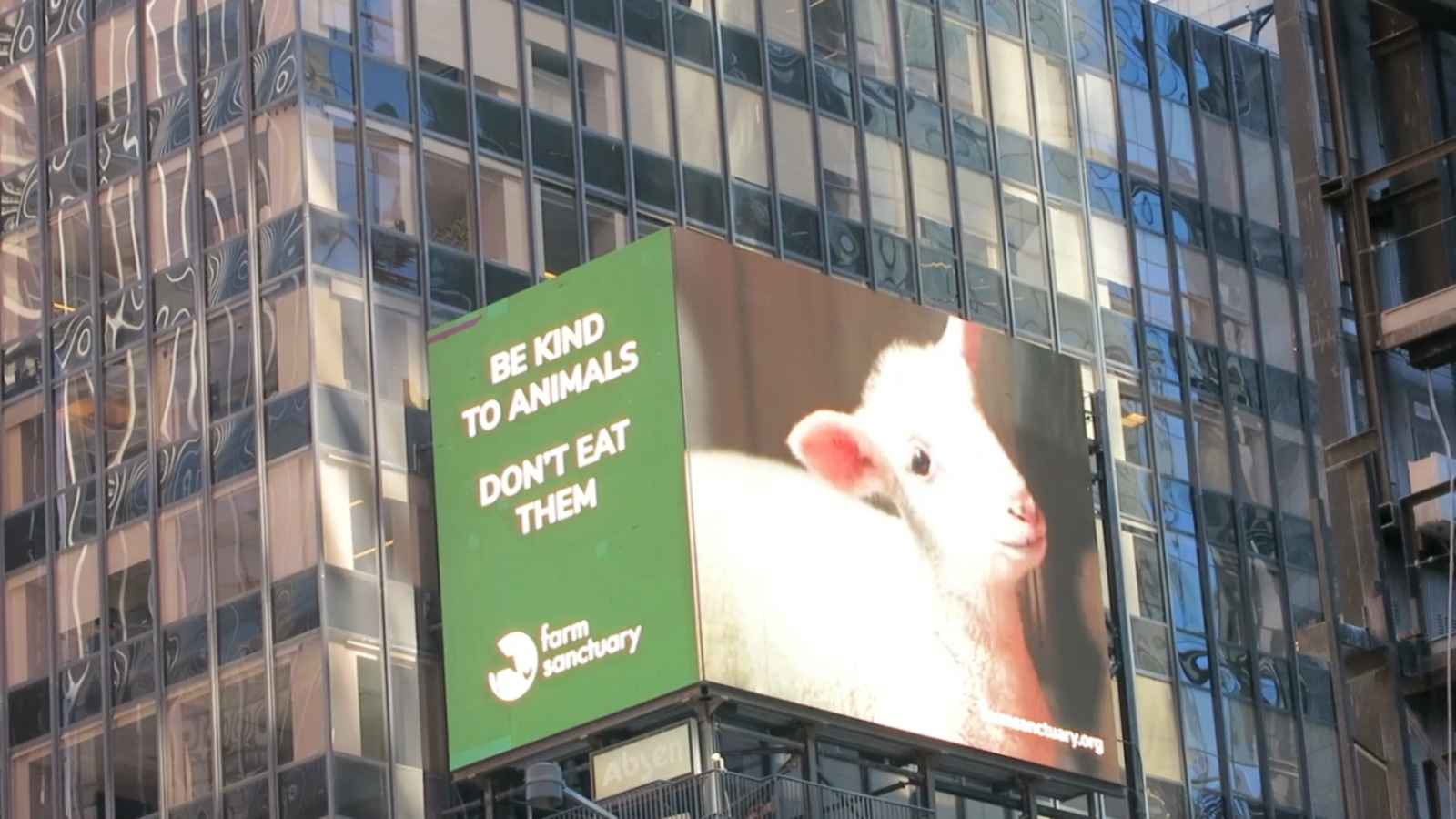 Billboard shows a green background with the words "Be kind to animals, don't eat them" and a Farm Sanctuary logo, next to a photo of a rescued lamb