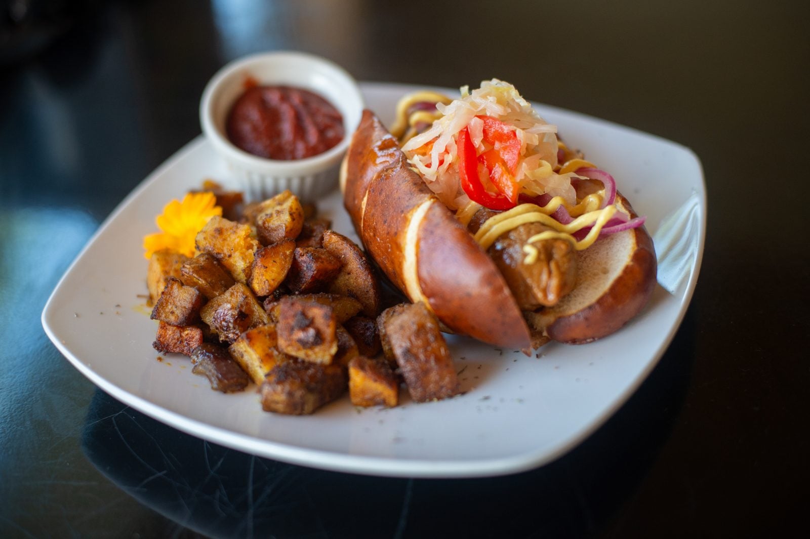 Vegan hot dog topped with jalapeno-apple sauerkraut and plated with potatoes and ketchup