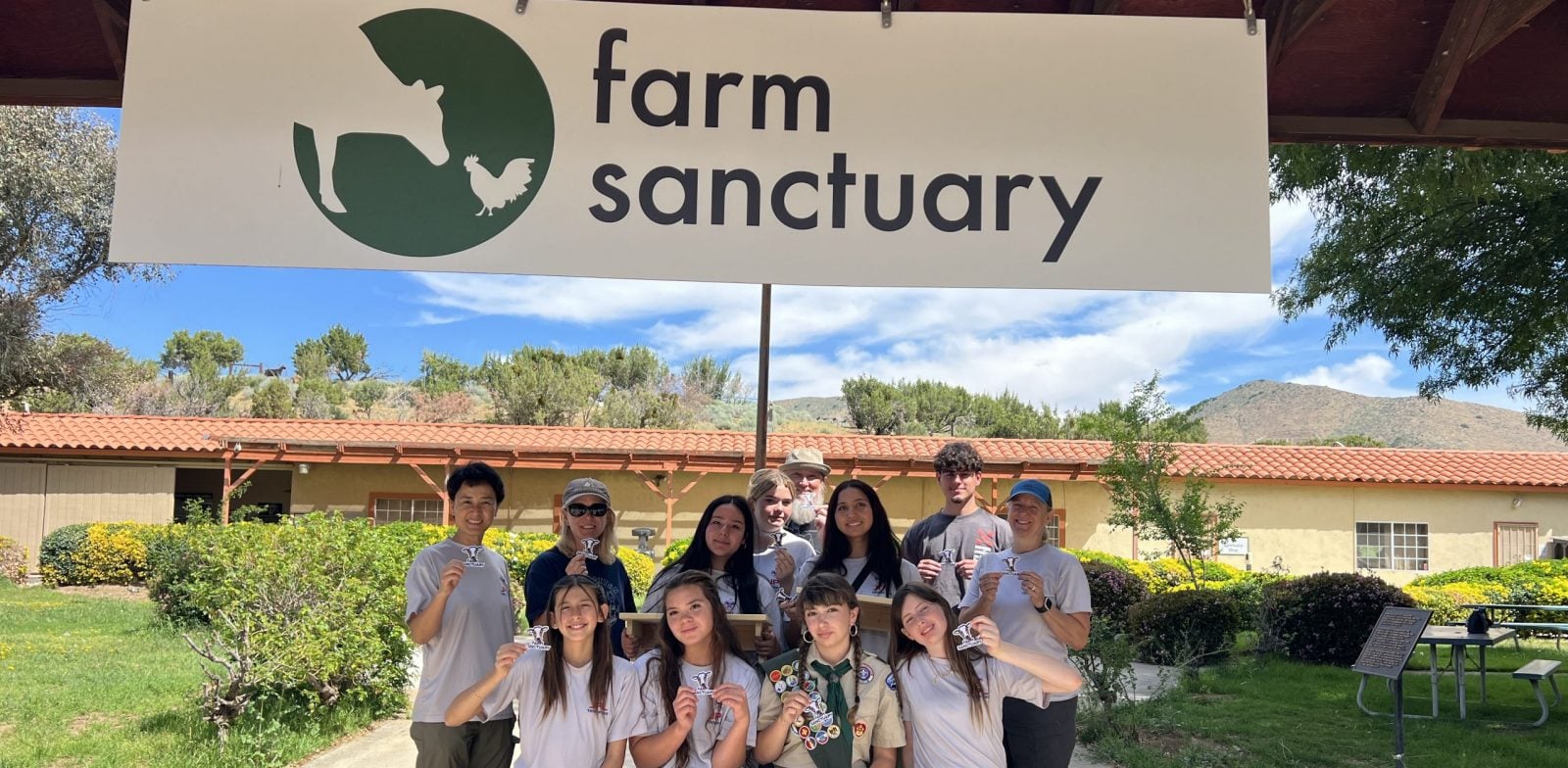 Troop of 12 Eagle Scouts sits on bench under Farm Sanctuary sign