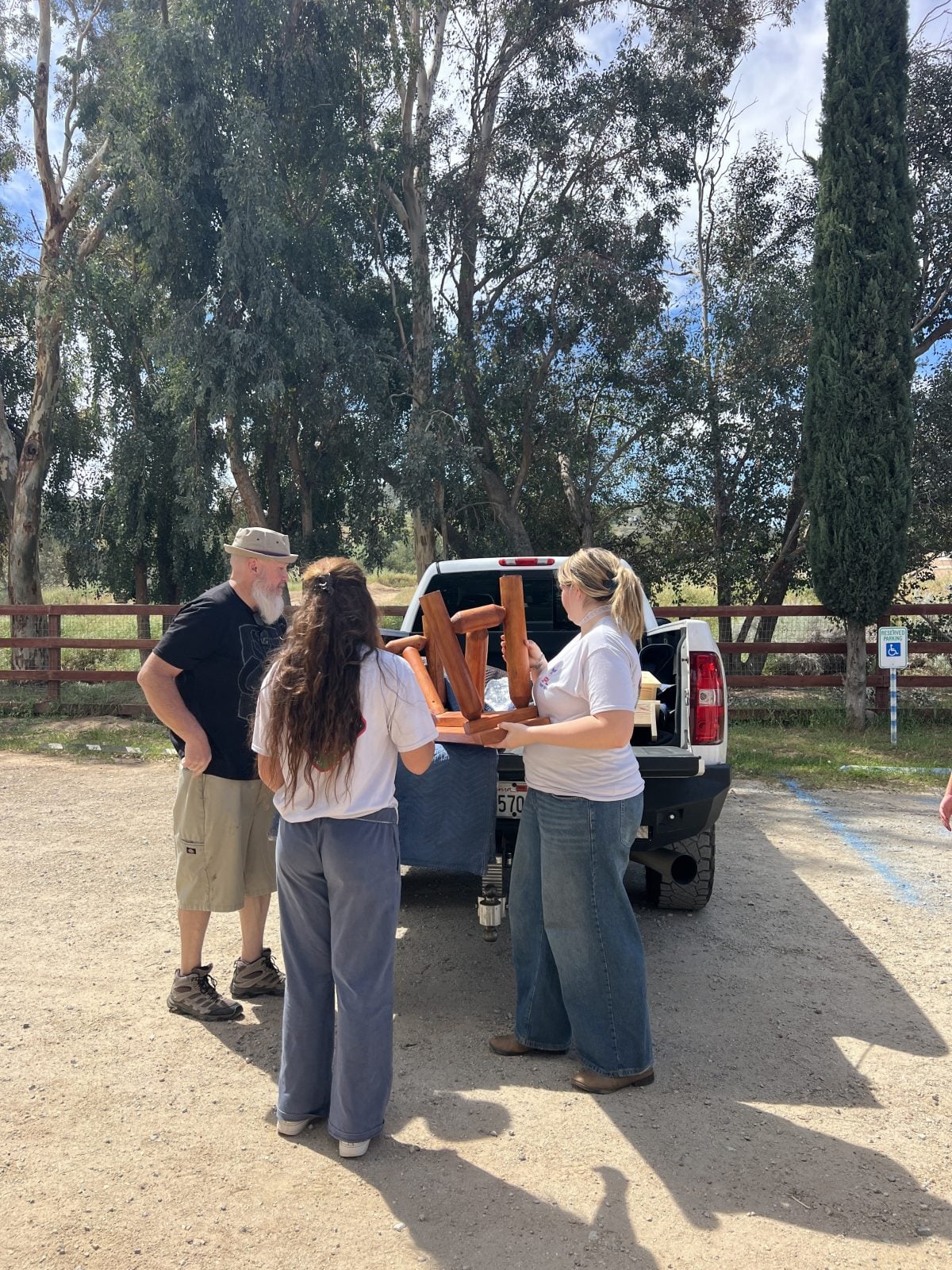 Three people lift a wooden bench out of a white truck at Farm Sanctuary