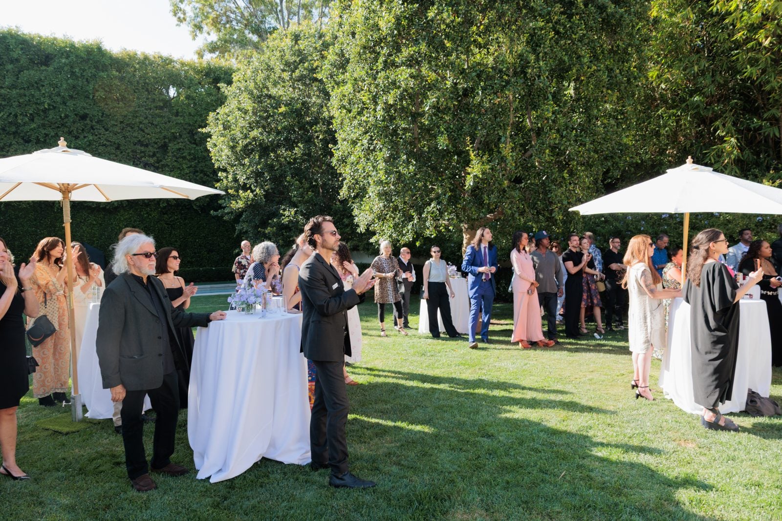 Guests clap at outdoor tables on a sunny day at a formal event
