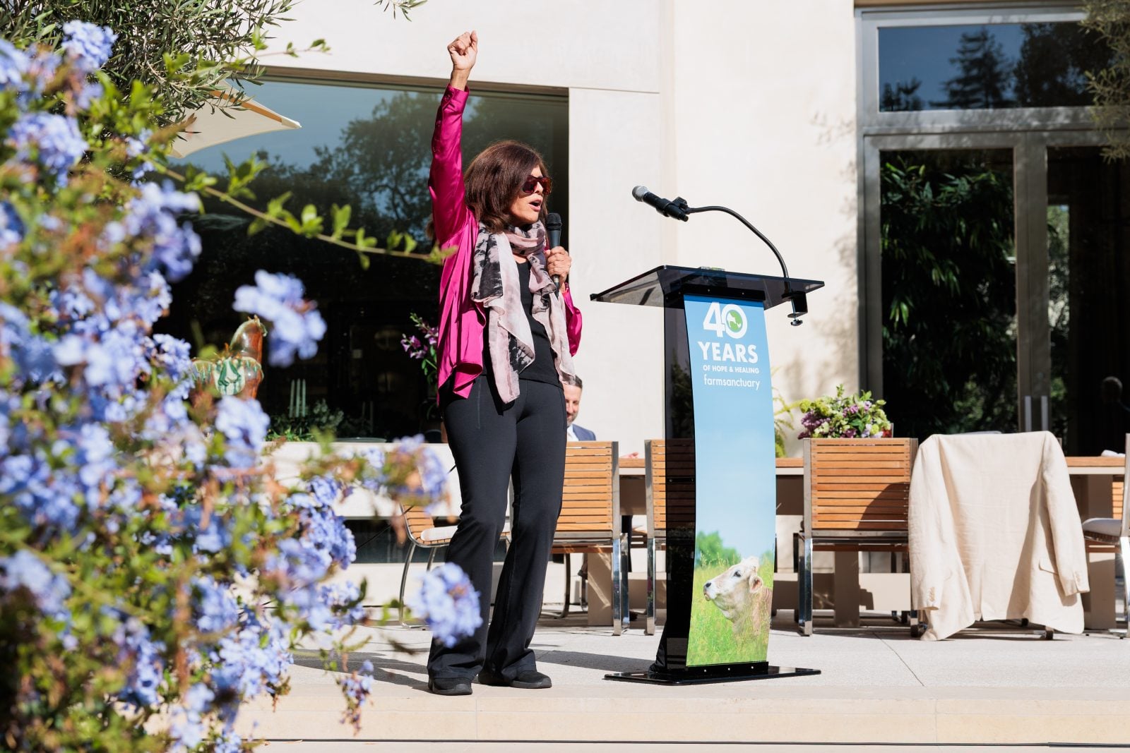 Jane Velez-Mitchell raises fist in the air while speaking into microphone on stage for Farm Sanctuary's 40th anniversary celebration