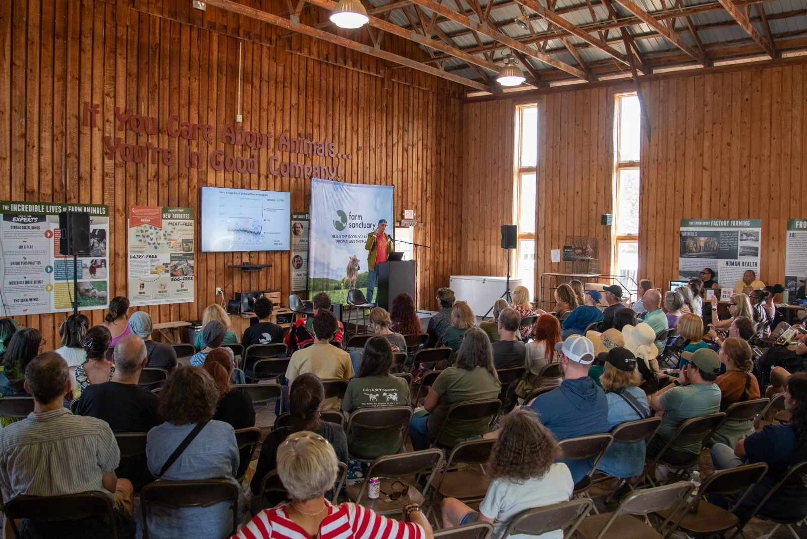 Pat Brown of Impossible Foods speaks in front of large crowd in Visitor Barn of Farm Sanctuary