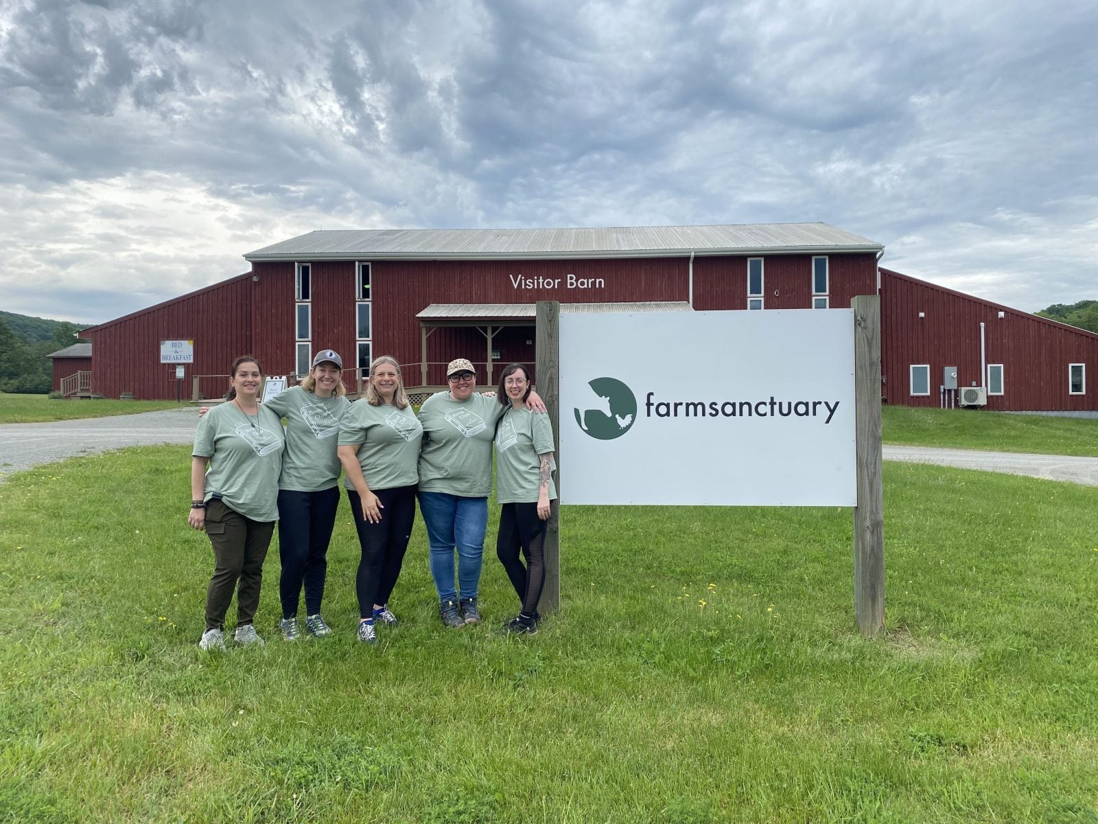Five visitors pose next to a "Farm Sanctuary" sign, in front of red "Visitor Barn"