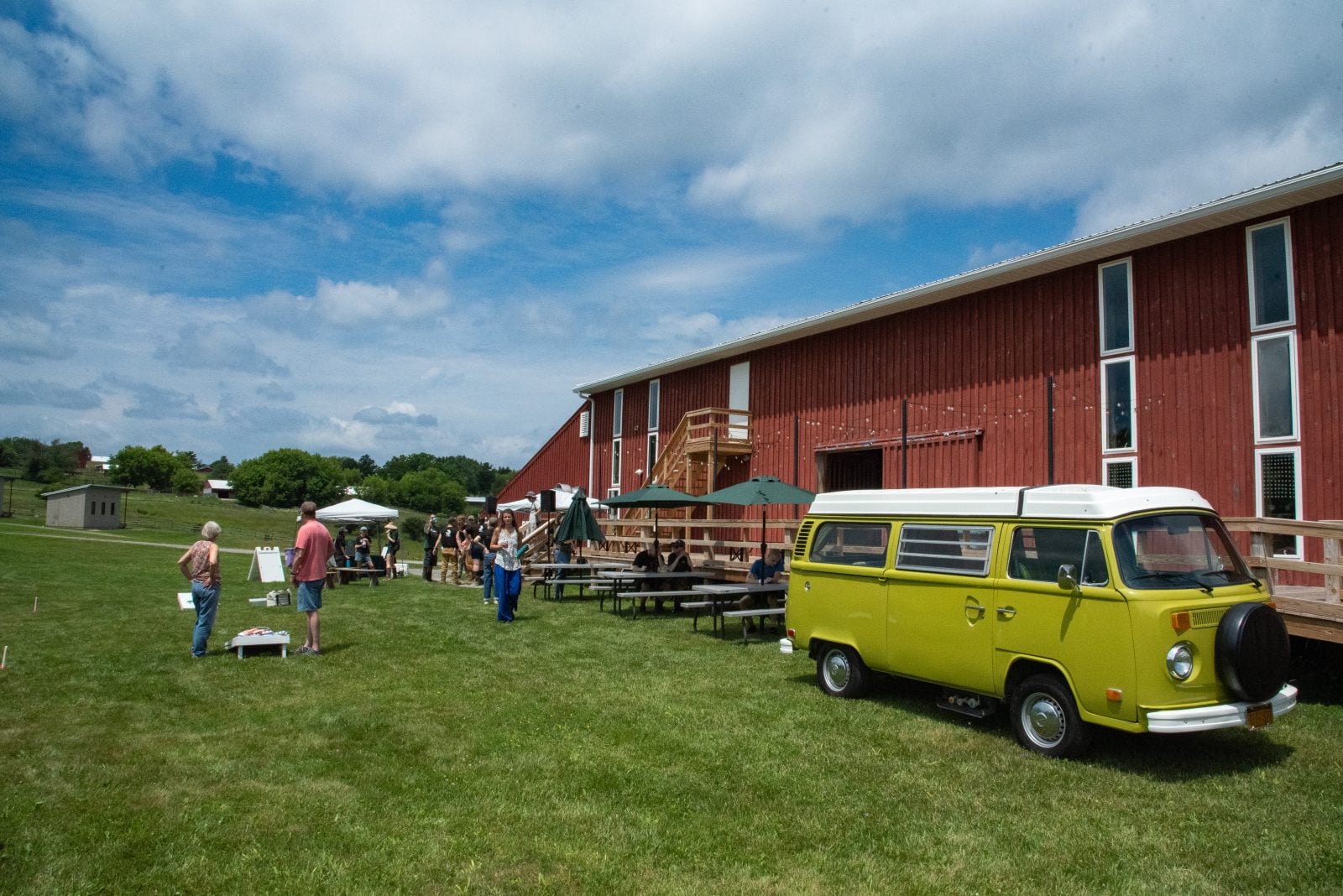 Guests of Farm Sanctuary's summer Pignic event stand near a green VW van parked outside a red barn
