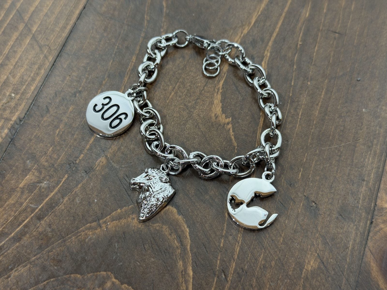 A silver bracelet with charms featuring the number 306, a sheep, and the Farm Sanctuary logo with a cow and chicken