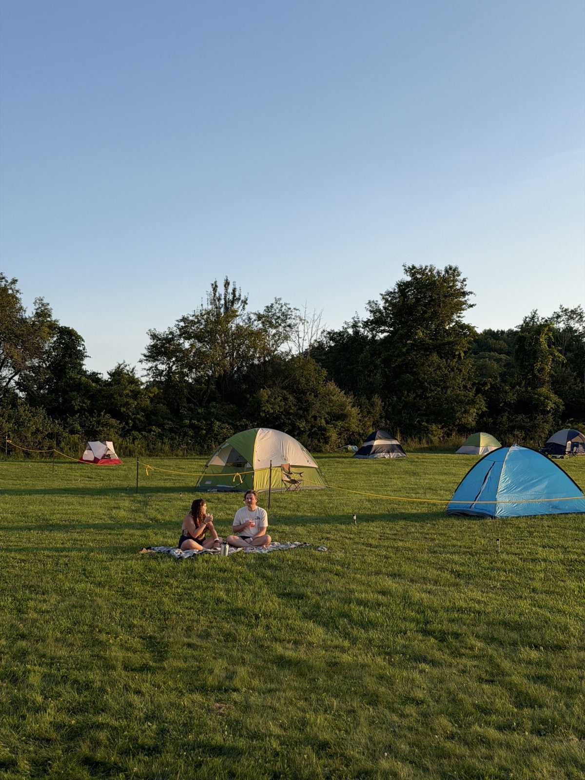 Two guests sit on blanket near camping tents in field at Farm Sanctuary