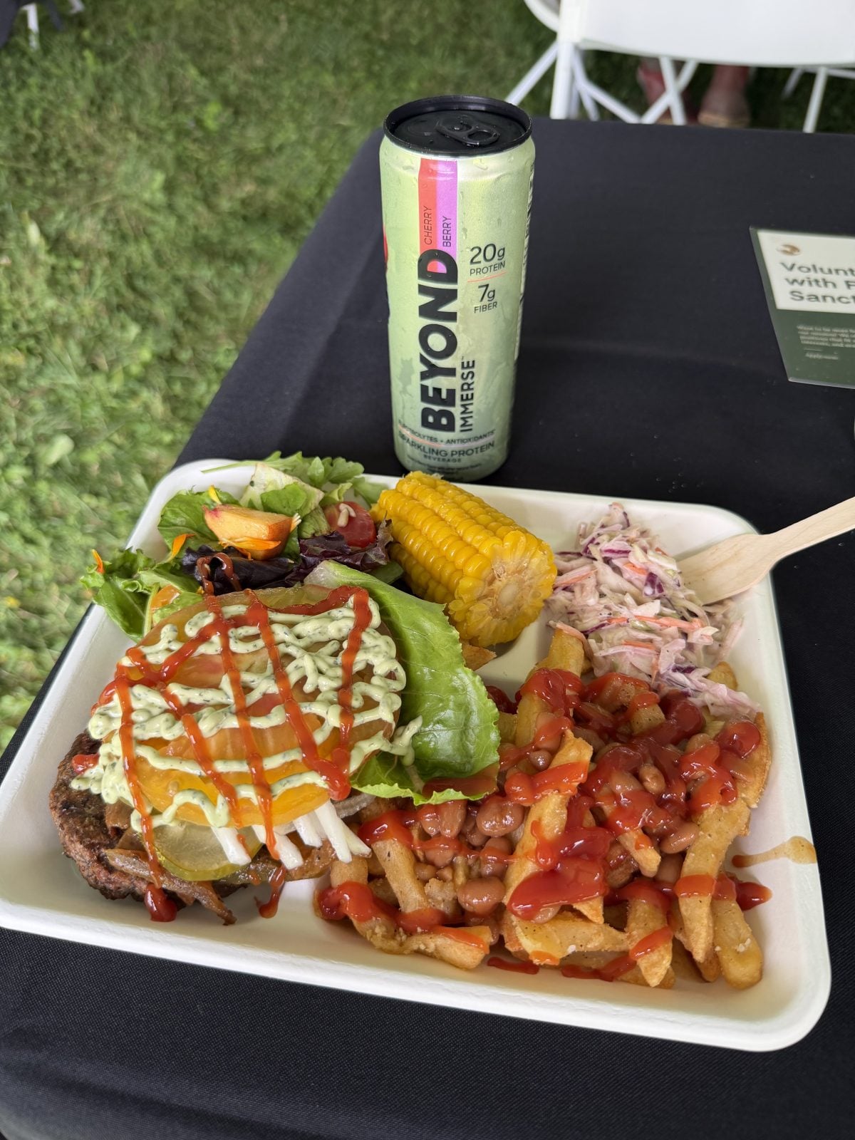 A plate of vegan food including a burger, fries, beans, slaw, and a salad sits on table next to can of Beyond Immerse