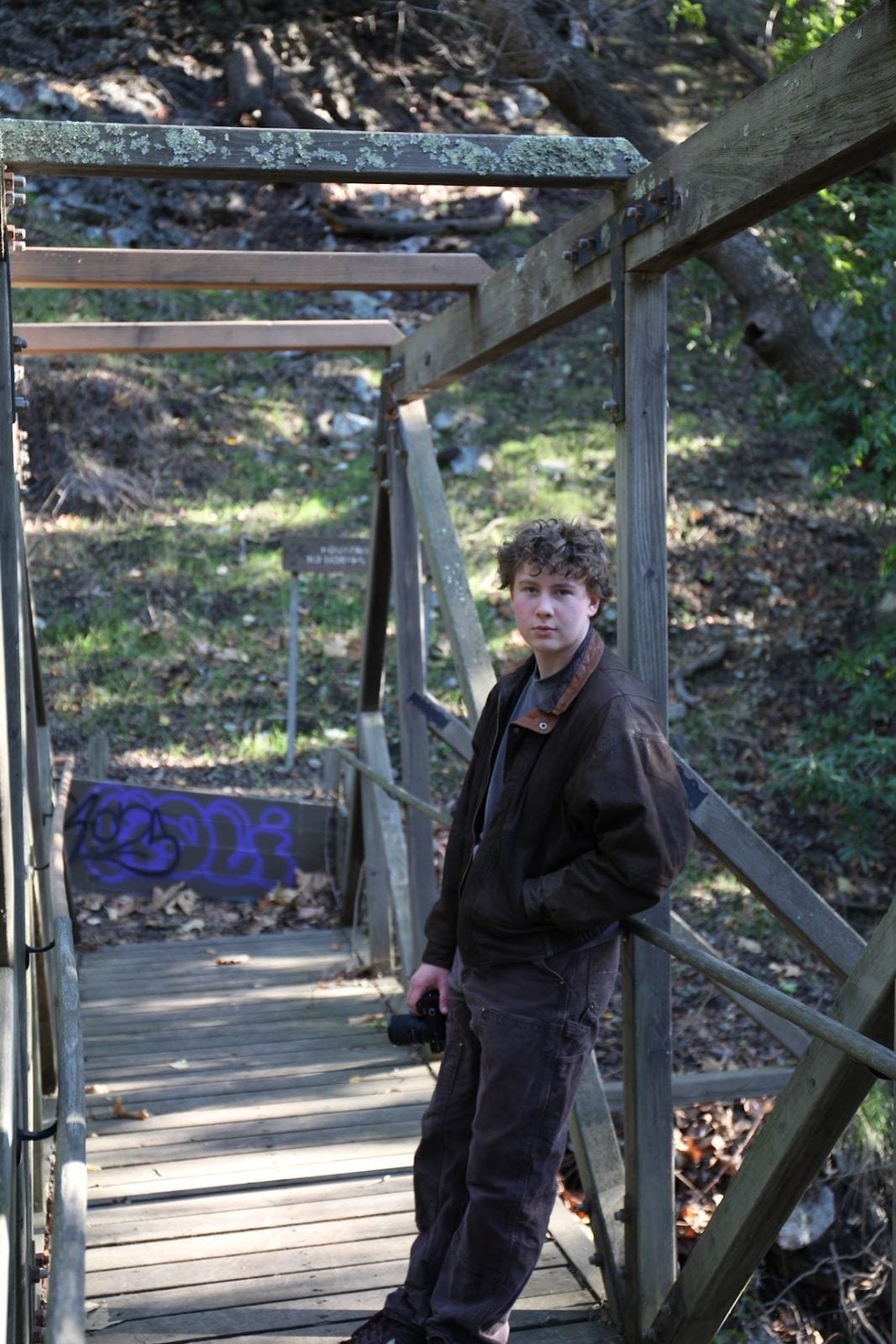 Young students stand on bridge holding camera