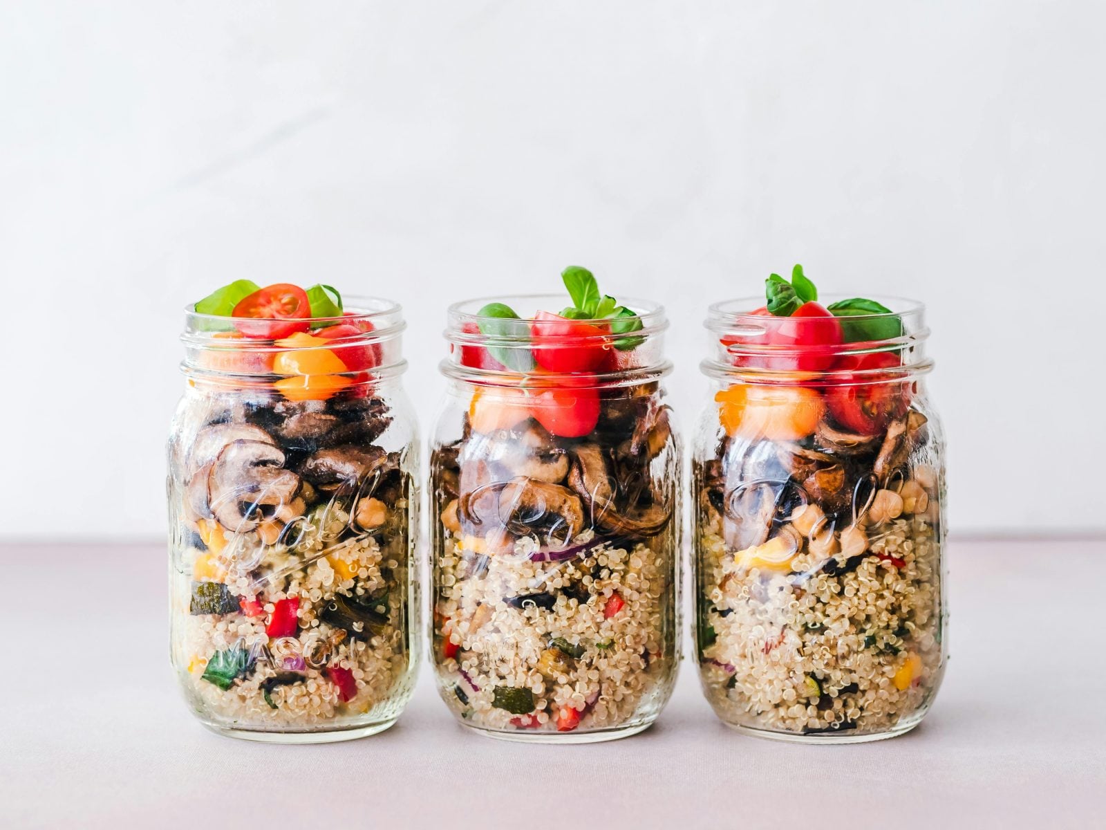 Three glass jars filled with quinoa, mushrooms, corn, tomatoes, and herbs